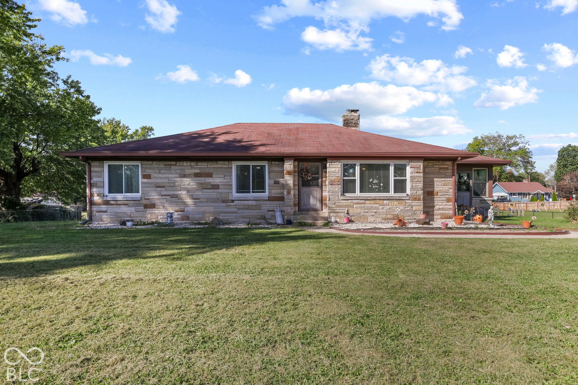 Stone veneer exterior with a red shingle roof, chimney, and multiple windows