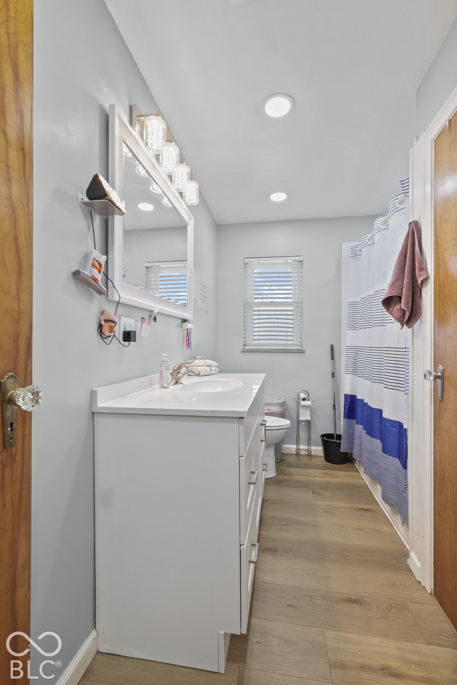 White vanity with integrated sink, wood-finish flooring, white window blinds, and recessed ceiling lighting