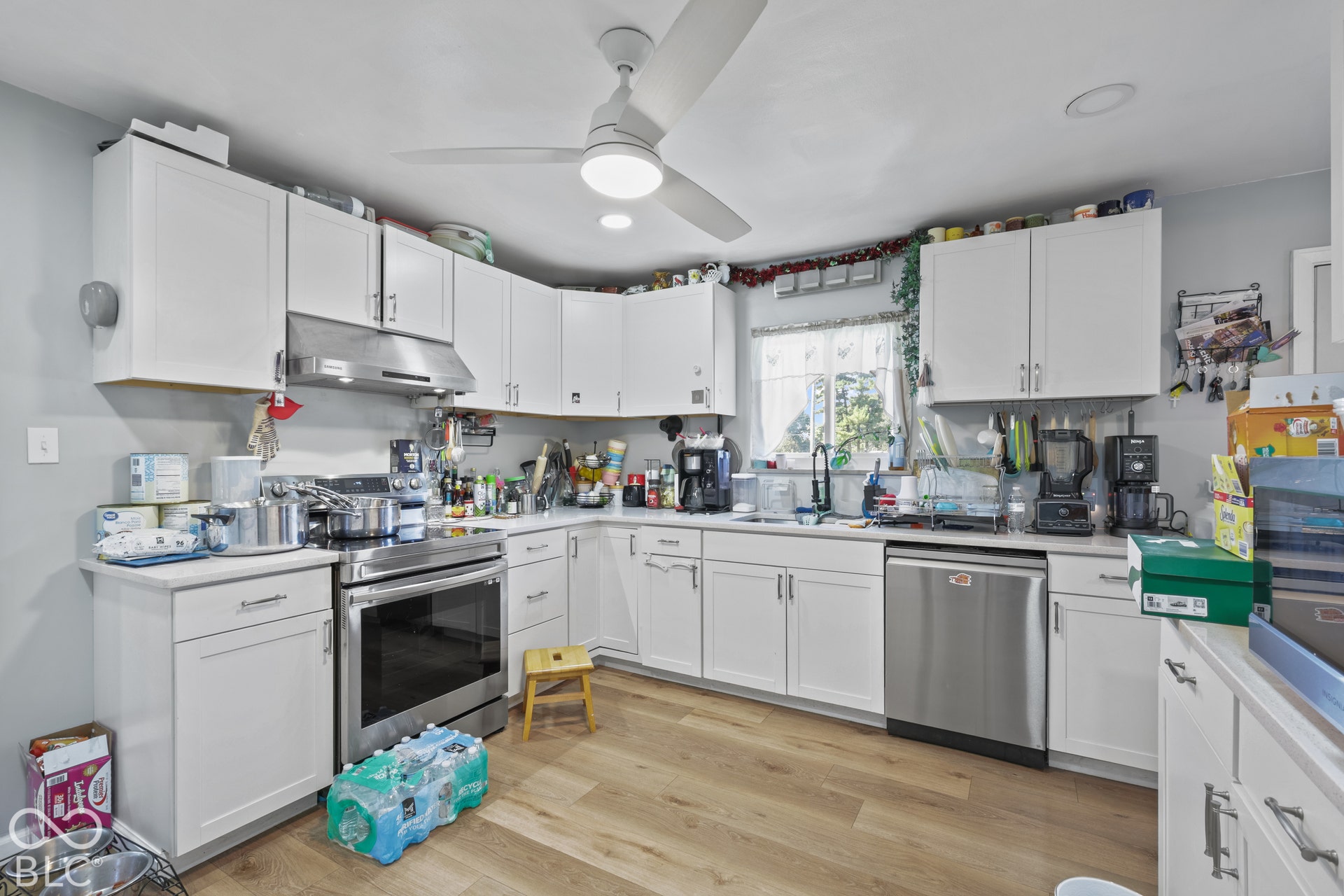 White shaker-style cabinetry, stainless steel appliances, wood-finish flooring, recessed lighting, and a ceiling fan