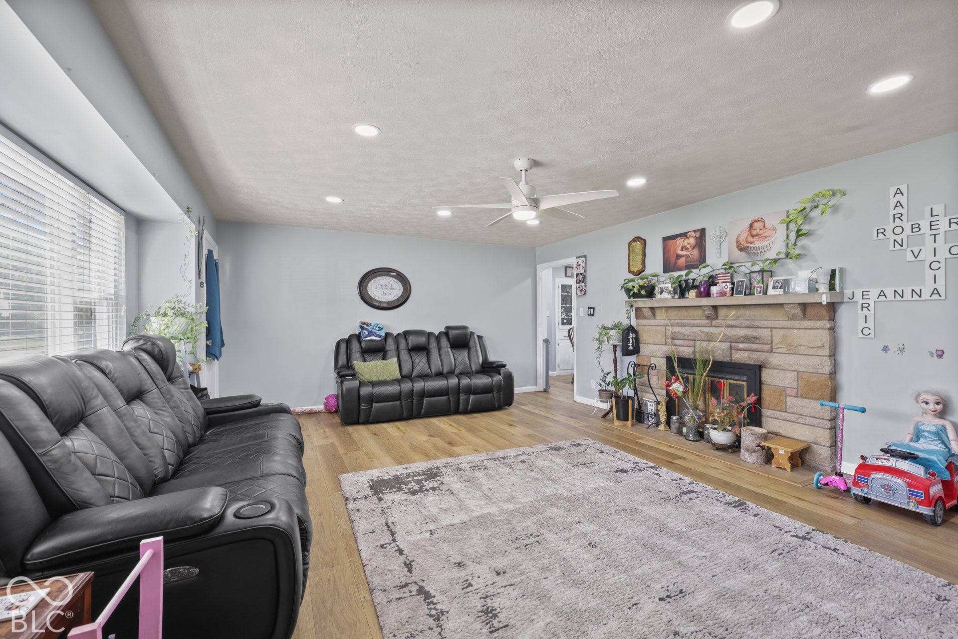 Stone-clad fireplace with mantel, recessed ceiling lighting, wood-finish flooring, and a ceiling fan