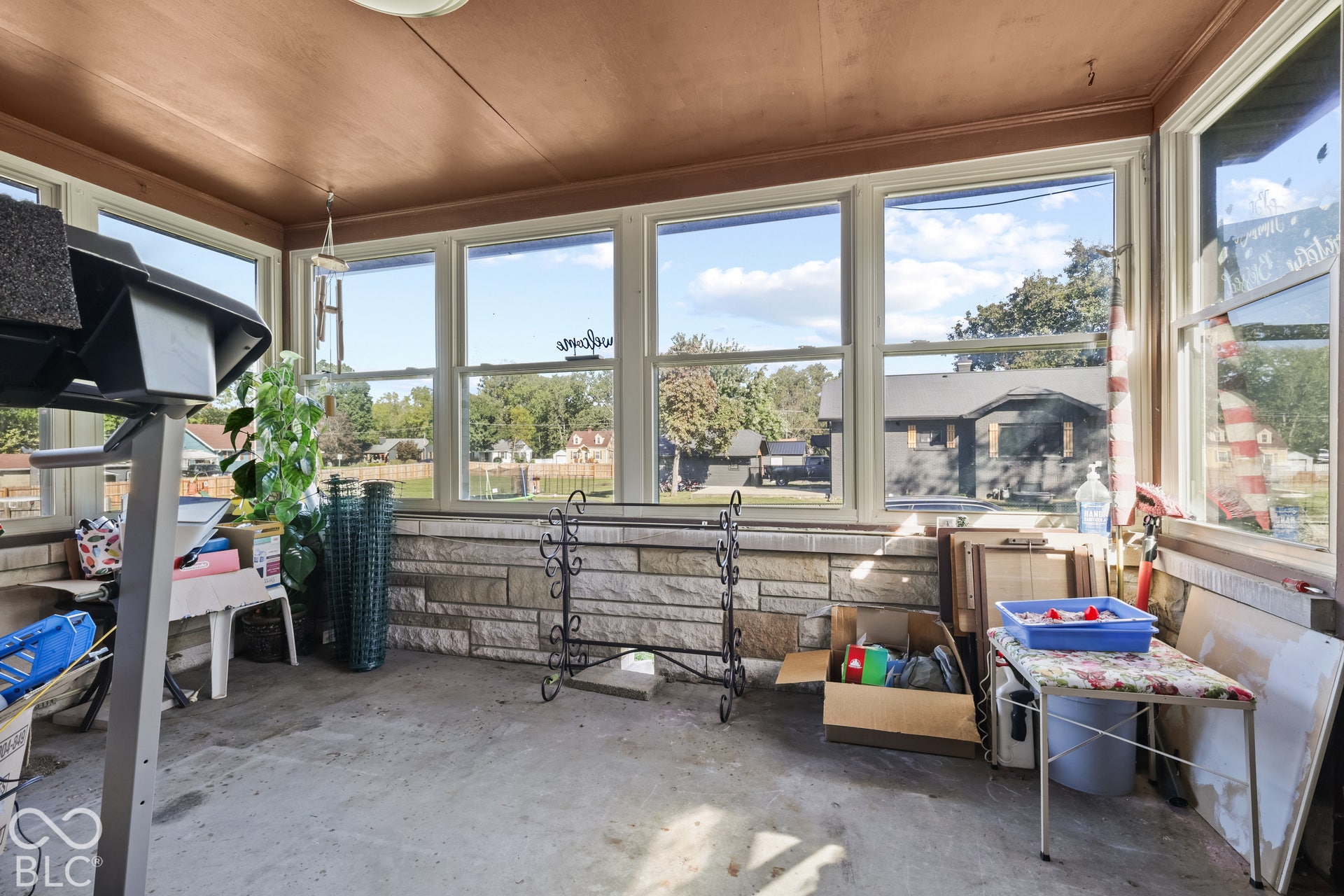 Enclosed porch featuring multiple windows, stone-finish half-walls, concrete flooring, and a ceiling fan