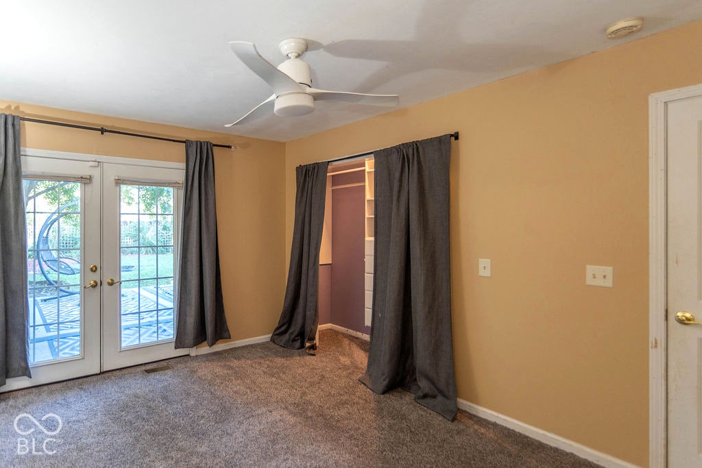 Dual French doors opening to the exterior, textured carpeting, a ceiling fan, and a built-in closet system