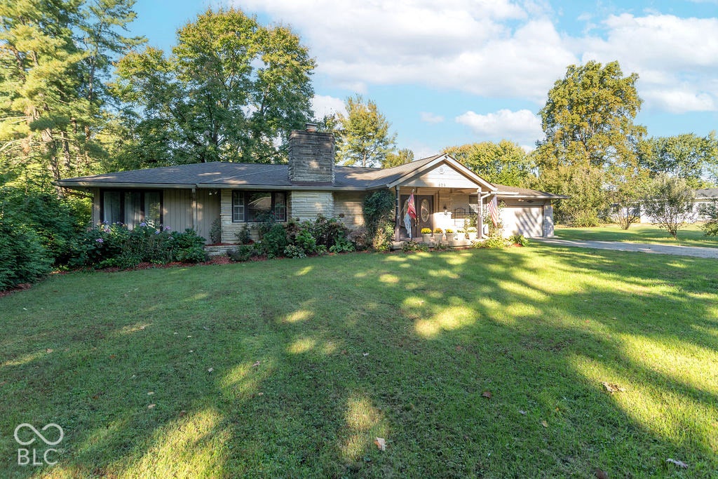 Ranch-style residence featuring a stone chimney, covered front porch, attached two-car garage, and established perimeter landscaping