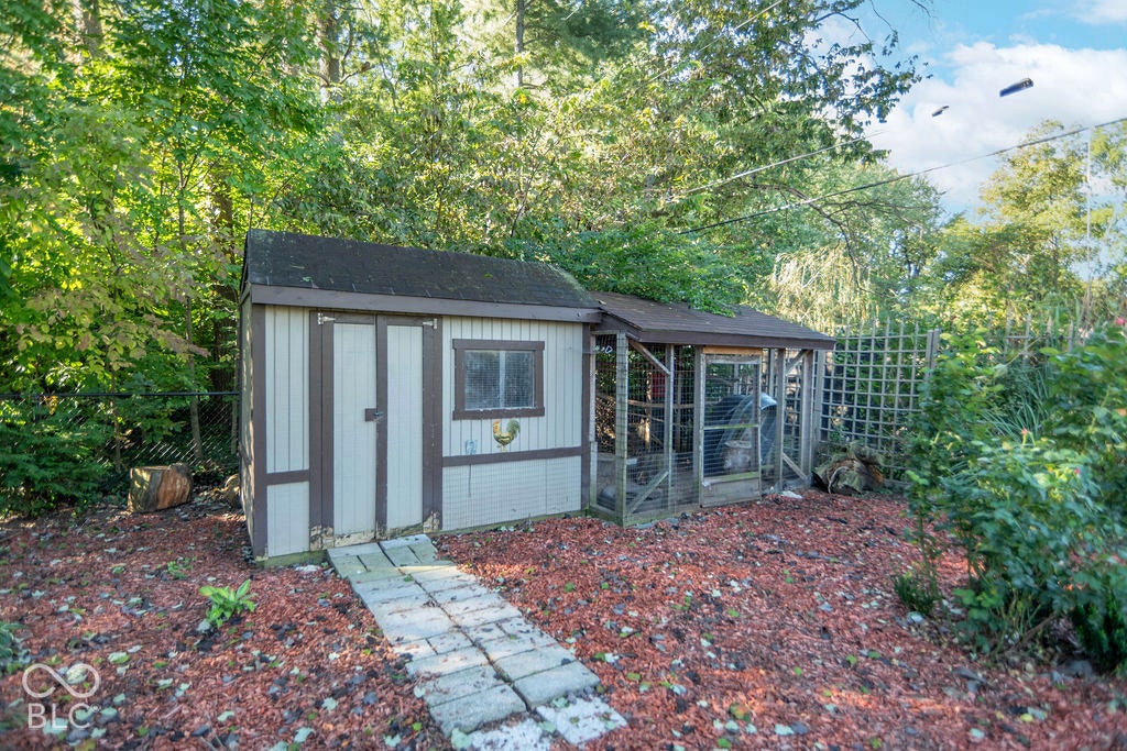 Outdoor storage shed with an attached aviary, featuring a concrete paver walkway, surrounded by mature trees and shrubs