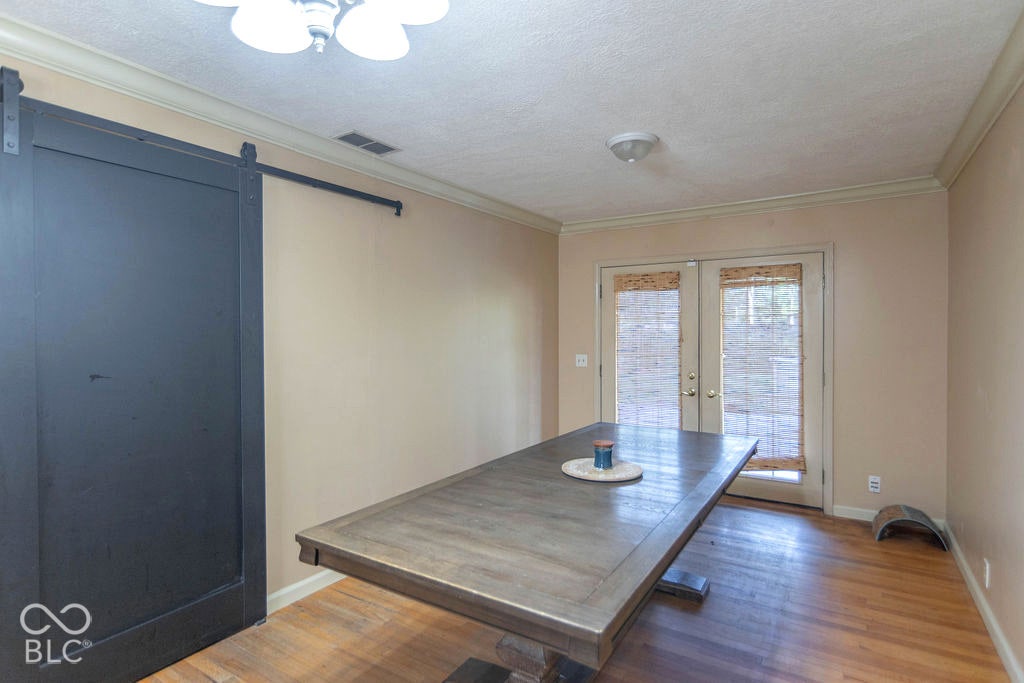 Wood-finish flooring, crown molding, and a dark-finished barn door on a black metal track