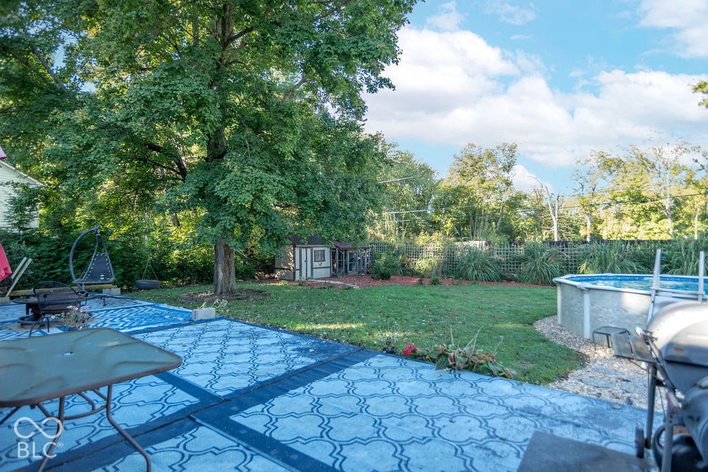 Paved patio area, expansive lawn, mature trees, privacy fencing, and an above-ground pool