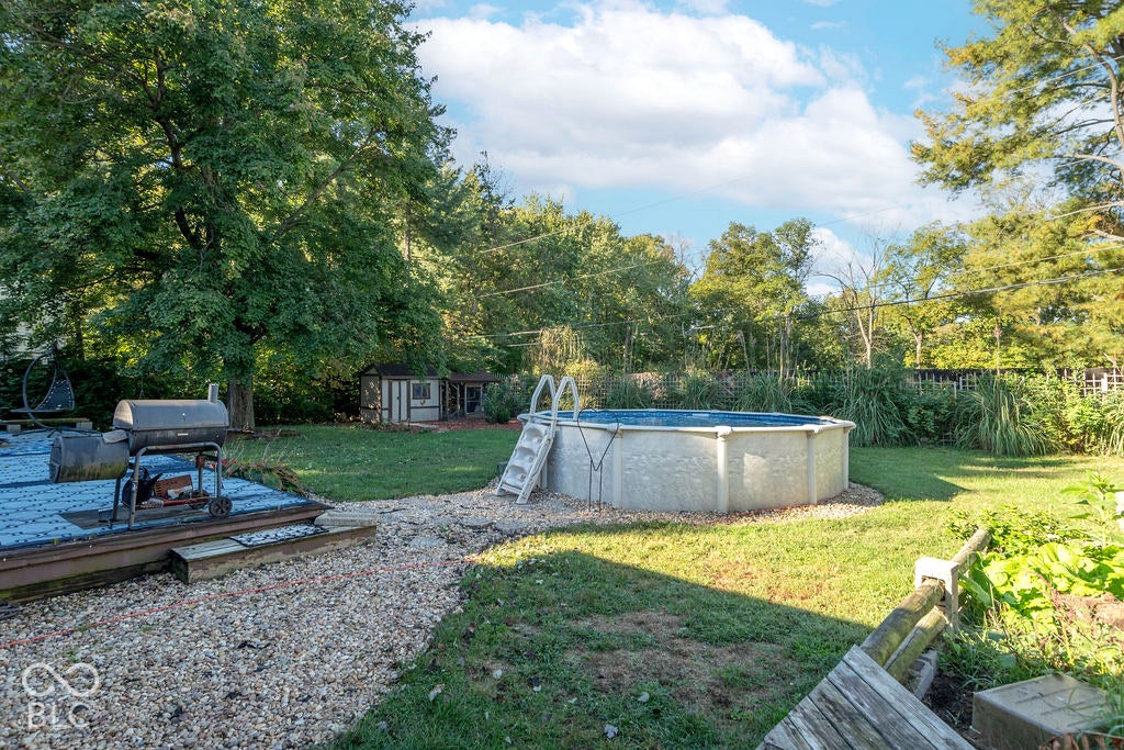 Expansive backyard featuring an above-ground pool, gravel pathways, a storage shed, and mature perimeter trees