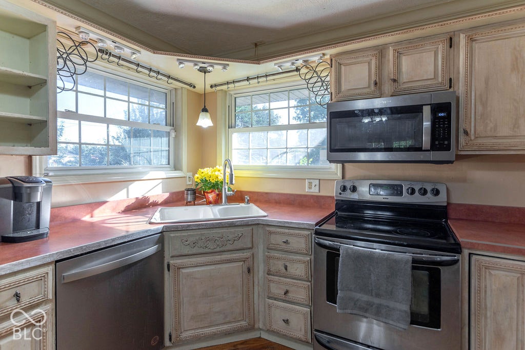 Kitchen featuring a double basin sink, stainless steel appliances, corner windows, and track lighting