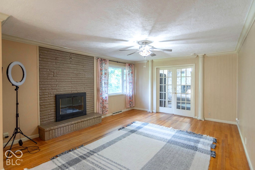Stone-face fireplace with hearth, wood-finish flooring, ceiling fan with integrated lighting, window with trim, and double glass-panel doors