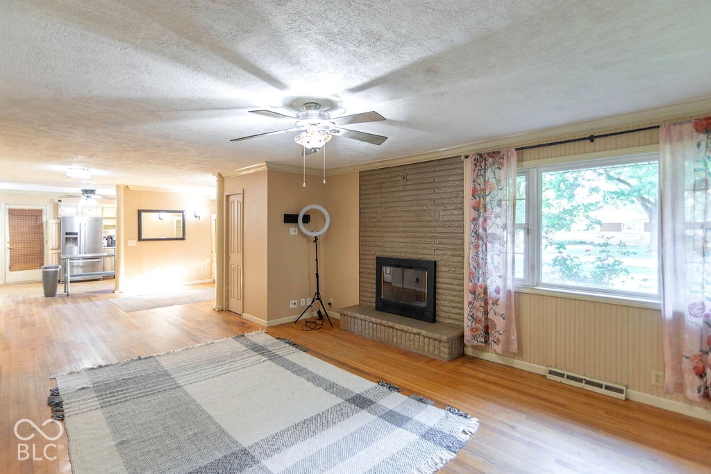 Hardwood flooring, a brick fireplace, a ceiling fan with integrated lighting, and a large window
