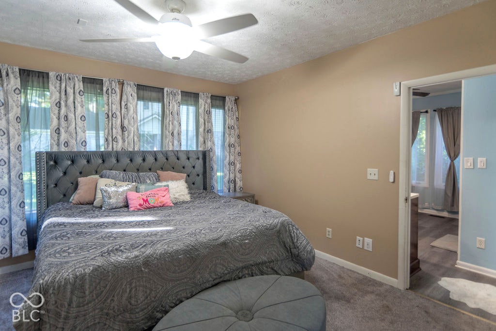 Light beige wall paint, ceiling fan with integrated lighting, multiple windows providing natural light, and a textured ceiling