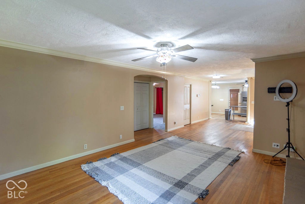 Hardwood flooring, crown molding, arched doorway, and a ceiling fan with integrated lighting