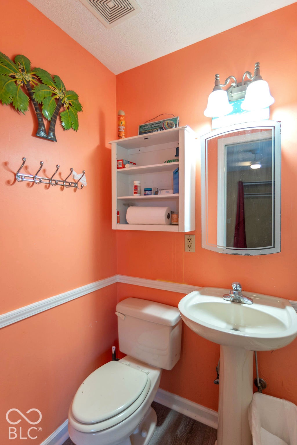 Pedestal sink with chrome faucet, wall-mounted mirror with integrated lighting, built-in shelving, and wood-finish flooring
