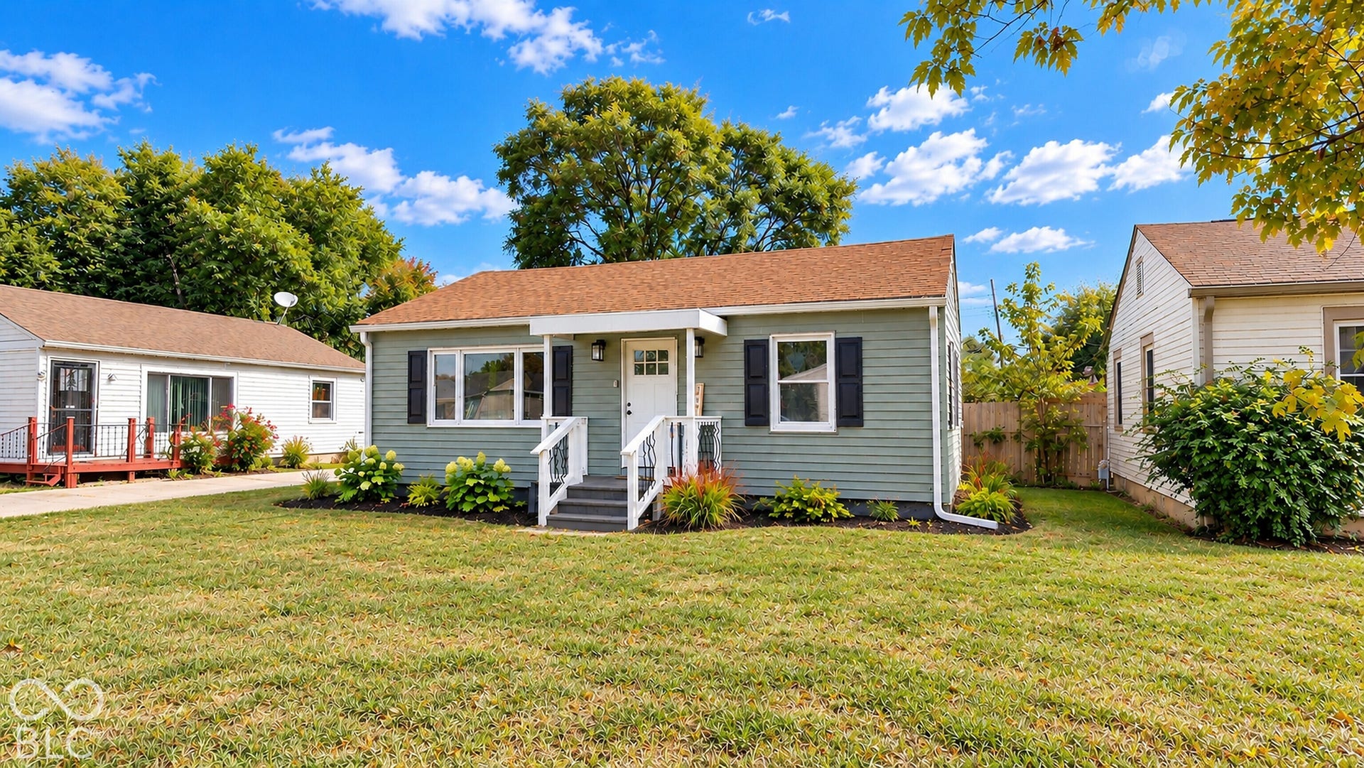 Virtually Altered - Single-story residence featuring light green siding, dark window shutters, and a front porch with white railings