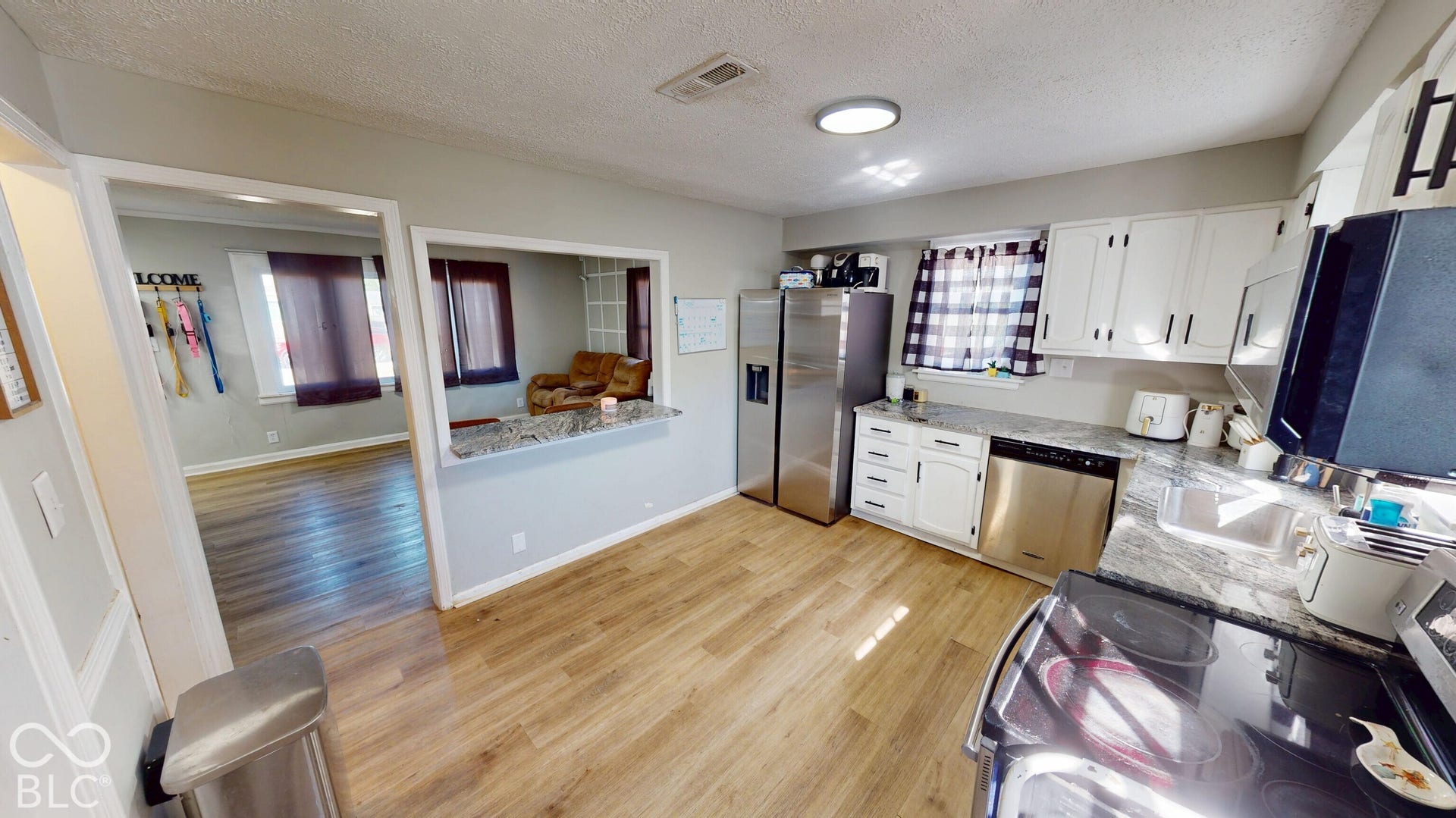 Kitchen featuring wood-finish flooring, white cabinetry, a built-in stainless steel dishwasher, a built-in stainless steel refrigerator, and stone-finish countertops