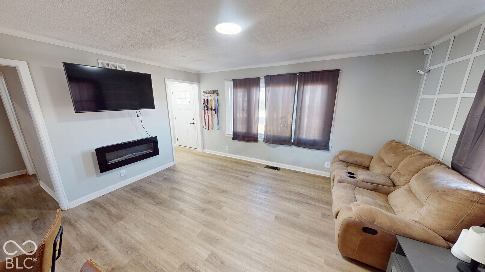 Wood-finish flooring throughout, integrated wall-mounted fireplace, multiple windows with dark-toned treatments, and decorative wall paneling