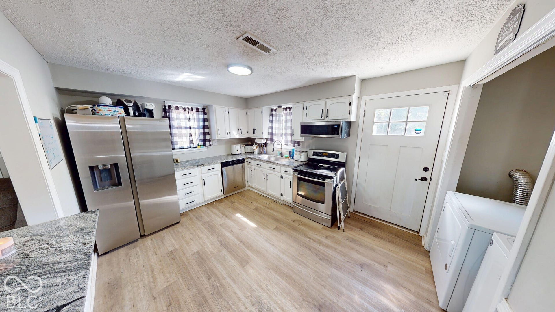 Kitchen featuring wood-finish flooring, white cabinetry, stainless steel appliances, and light-toned countertops