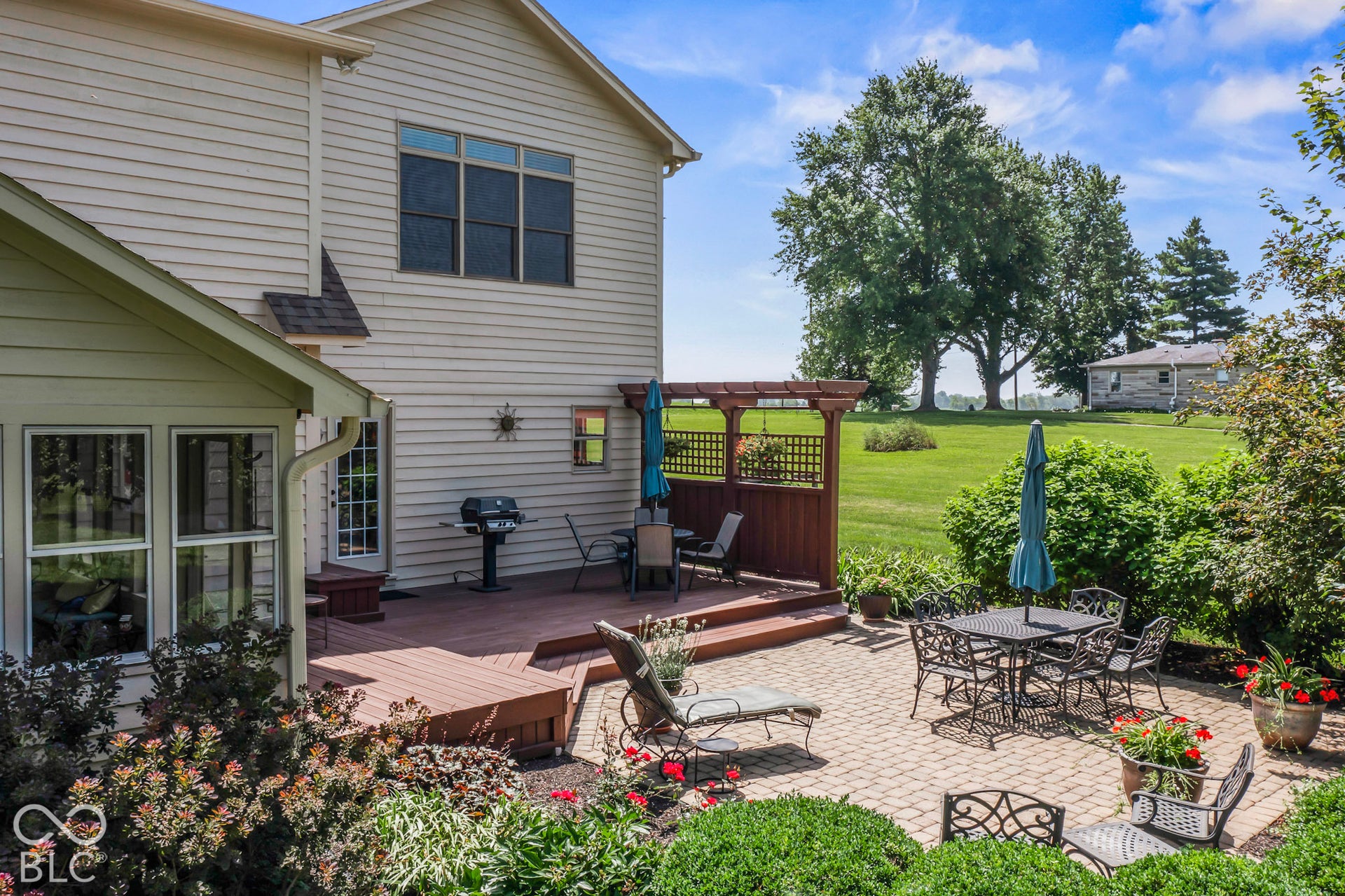 10954 N County Road 150 Road E, Pittsboro, IN 46167 Multi-level wood-finish deck featuring a built-in pergola and adjoining paver patio, surrounded by mature landscaping and expansive green space