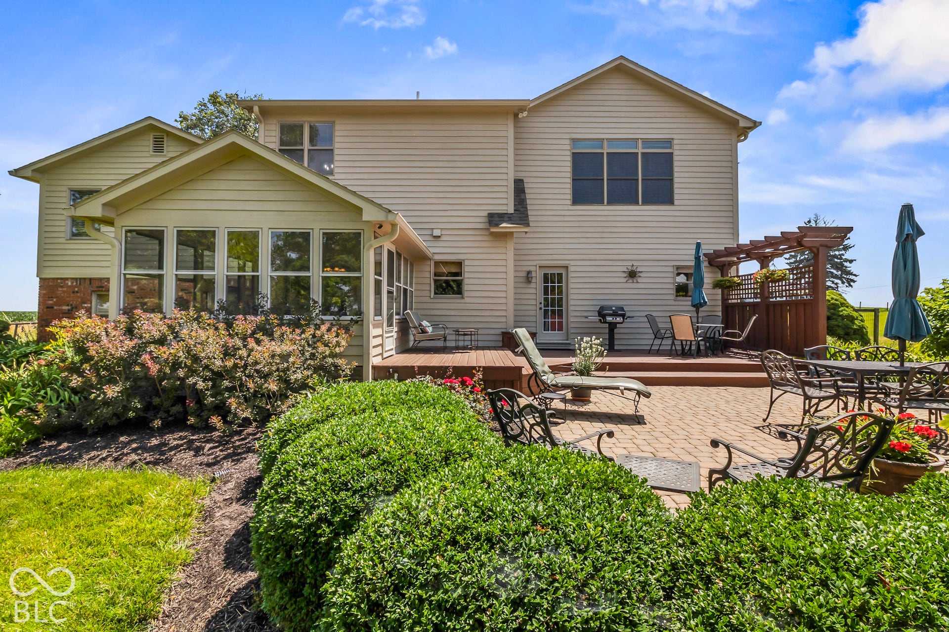 10954 N County Road 150 Road E, Pittsboro, IN 46167 Multi-level home exterior featuring a rear paved patio, elevated wood deck, and enclosed sunroom, accented by a wood pergola and mature landscaping