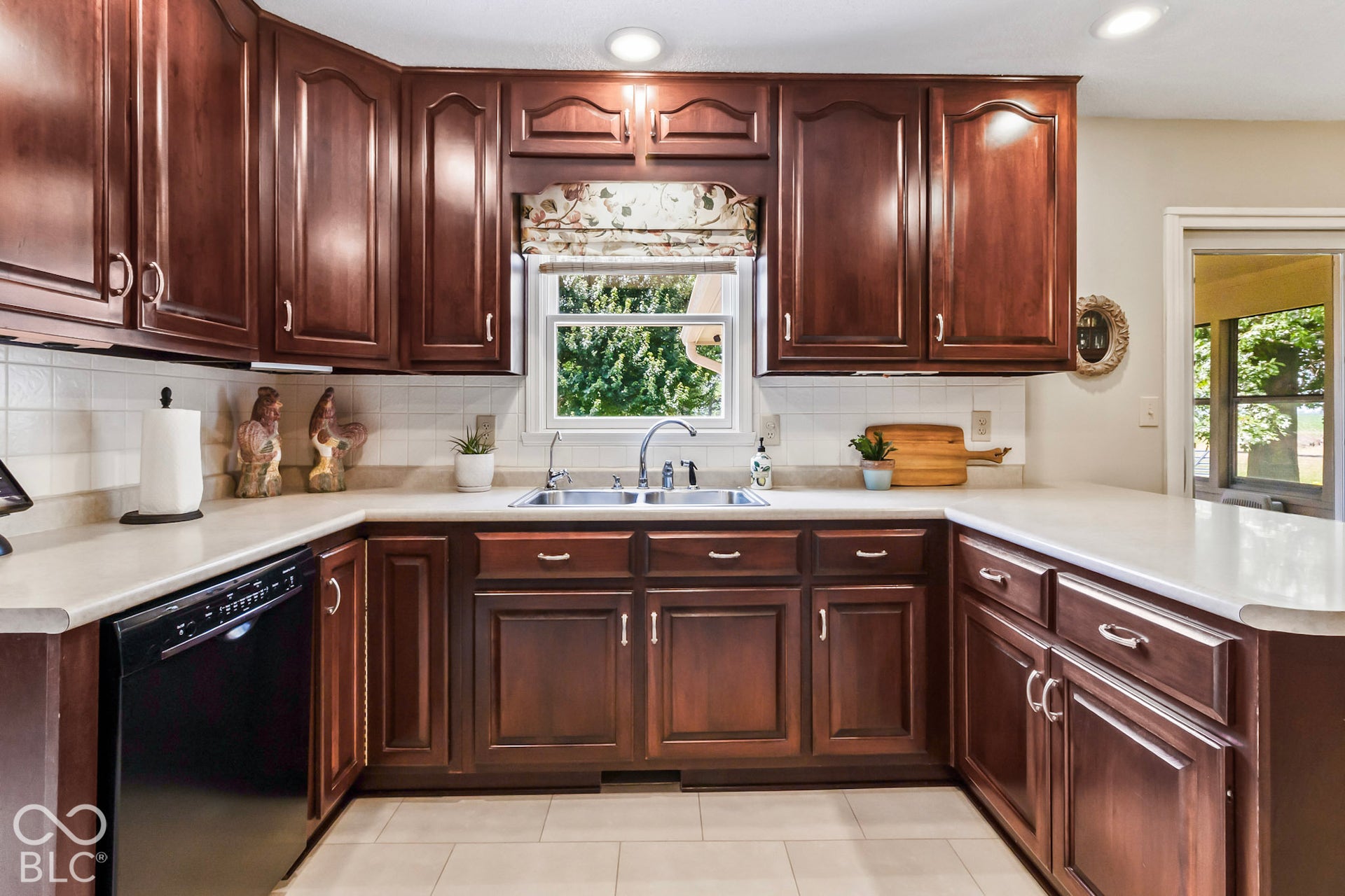 10954 N County Road 150 Road E, Pittsboro, IN 46167 Kitchen featuring raised-panel wood cabinetry, solid-surface countertops, a double-basin stainless steel sink, a tiled backsplash, and neutral tile flooring