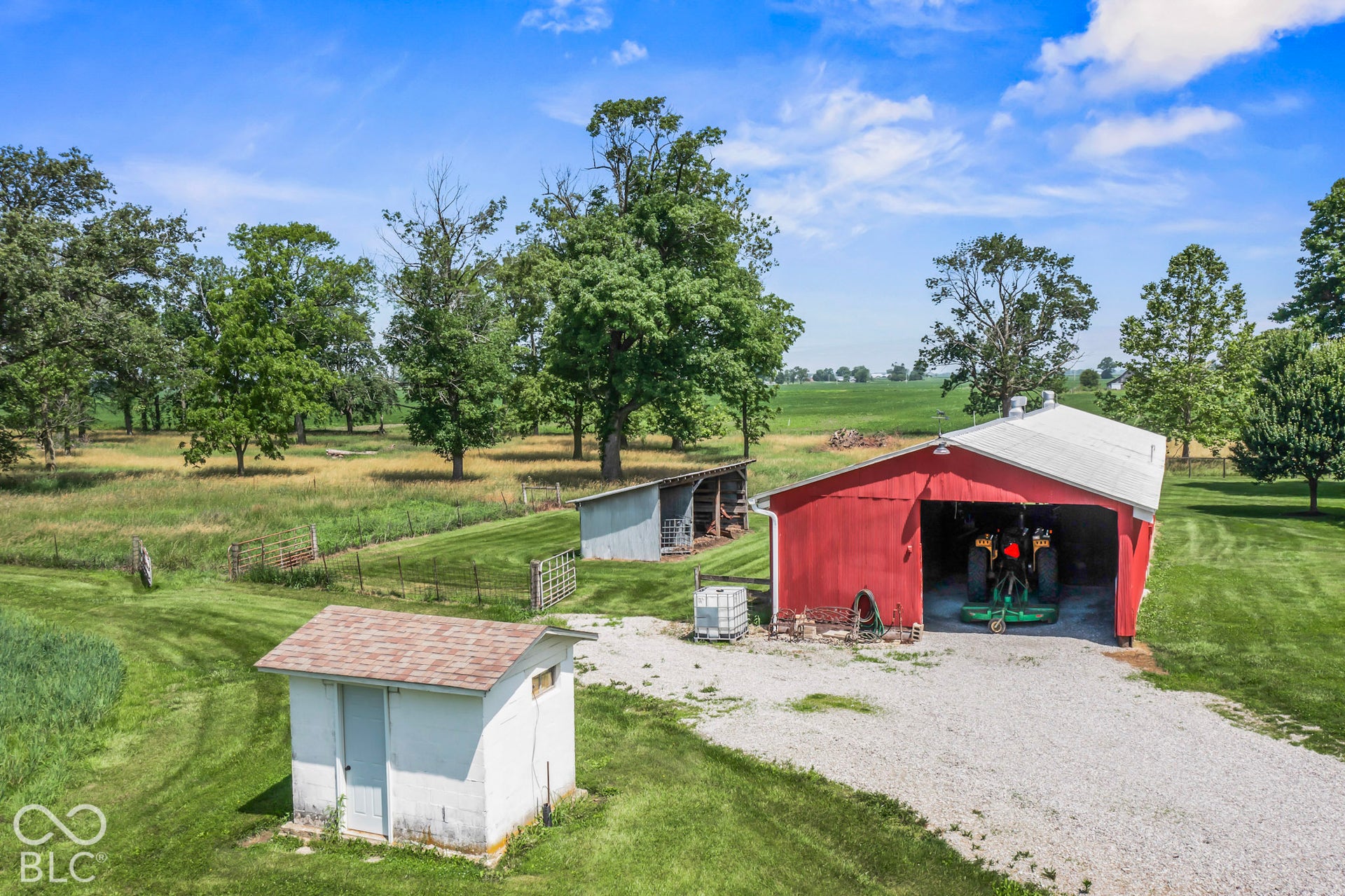 10954 N County Road 150 Road E, Pittsboro, IN 46167 Expansive grounds featuring a red-sided barn, a detached concrete block utility building, a gravel driveway, and mature trees
