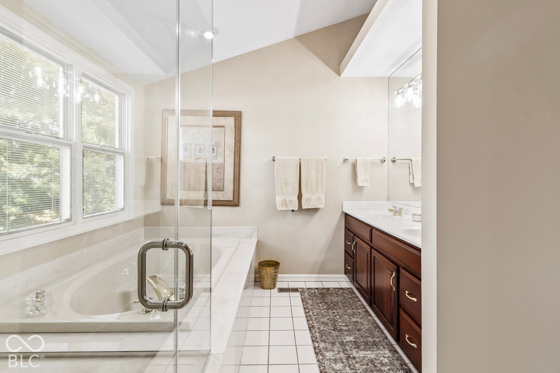 10954 N County Road 150 Road E, Pittsboro, IN 46167 Bathroom featuring a dual-sink vanity with dark-finish cabinetry, white tile flooring, a separate soaking tub with a surrounding deck, and a glass-enclosed shower area under a vaulted ceiling