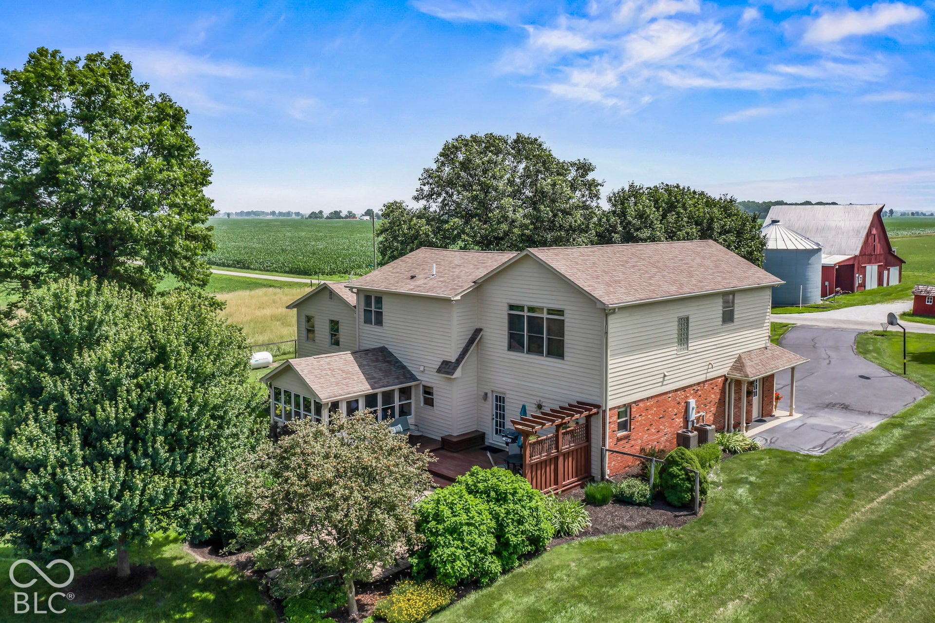 10954 N County Road 150 Road E, Pittsboro, IN 46167 Two-story exterior with light siding and brick lower-level facade, featuring an attached sunroom, wood pergola, expansive acreage, and a detached barn structure