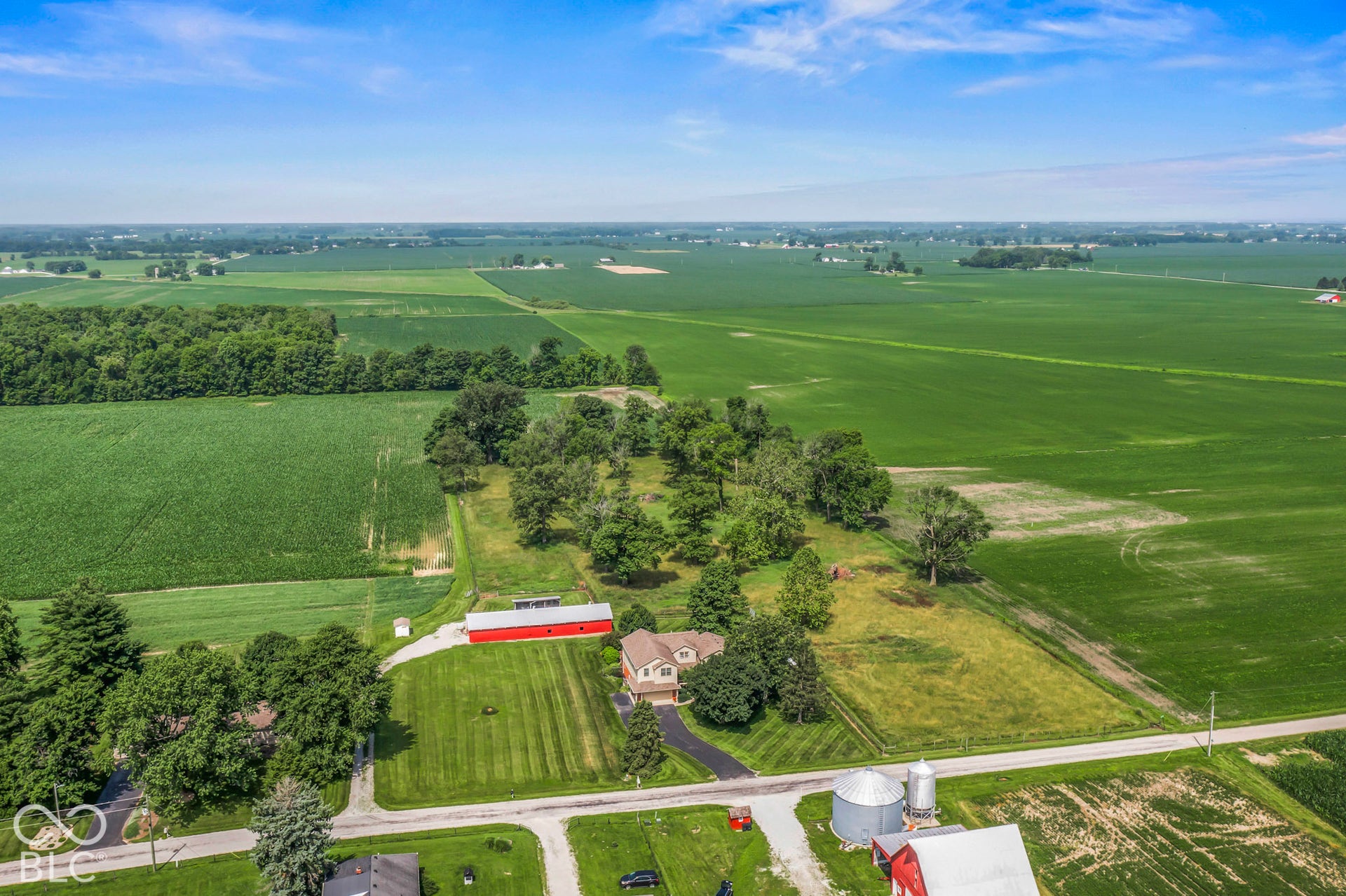 10954 N County Road 150 Road E, Pittsboro, IN 46167 Aerial acreage featuring expansive agricultural fields, mature trees, a detached red barn, and two metal grain silos