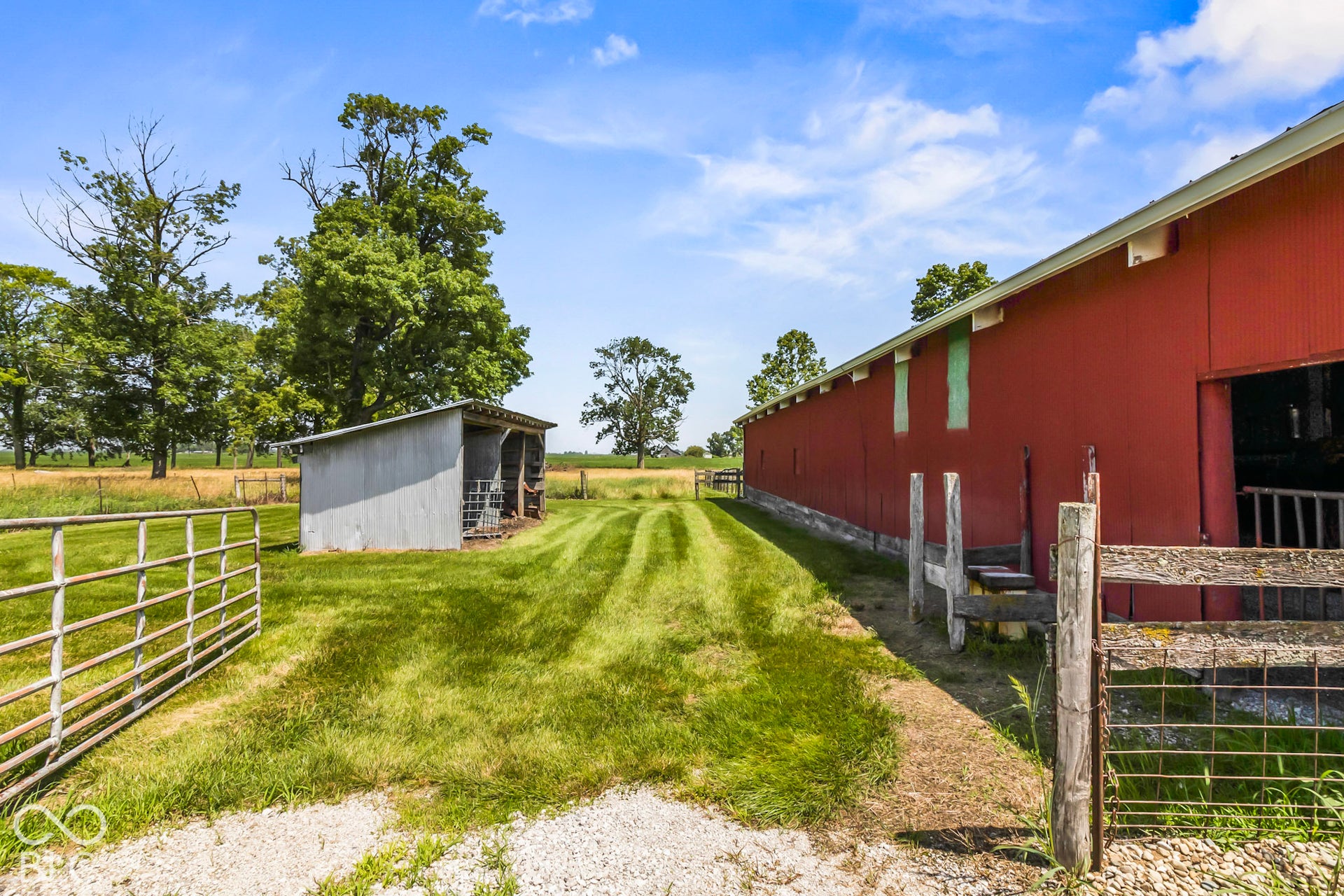 10954 N County Road 150 Road E, Pittsboro, IN 46167 Red exterior barn featuring metal siding, open-air storage structure, fenced perimeter, and expansive grass acreage