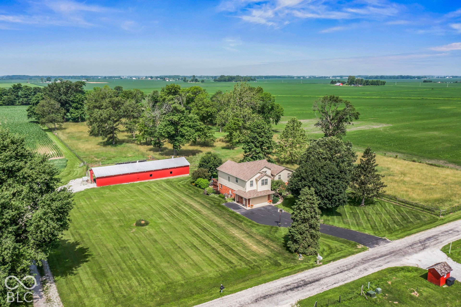10954 N County Road 150 Road E, Pittsboro, IN 46167 Aerial perspective featuring a multi-story residence, a large red outbuilding with a metal roof, expansive lawn, paved driveway, and mature tree clusters