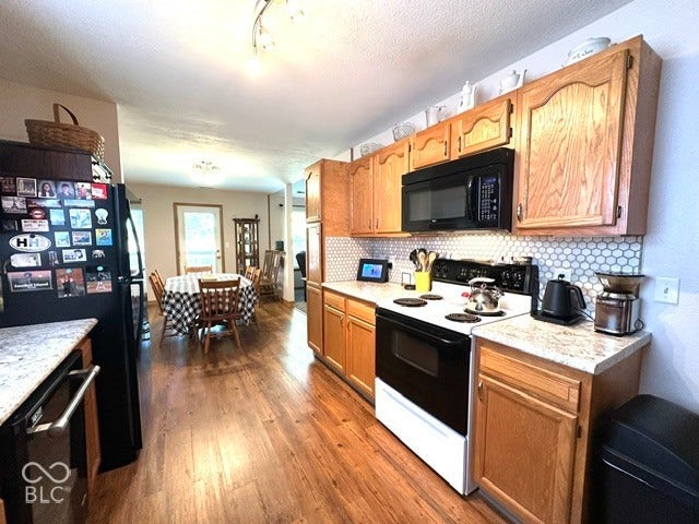 1712 Austin Drive, Lebanon, IN 46052 Kitchen featuring wood-finish flooring, light-toned cabinetry, light-colored countertops, a white hexagon tile backsplash, and a black over-the-range microwave