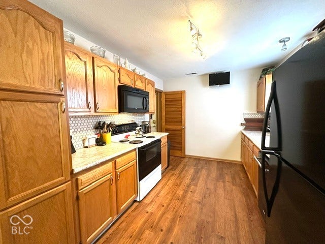 1712 Austin Drive, Lebanon, IN 46052 Wood-finish flooring, light wood cabinetry, white hexagonal tile backsplash, light-toned countertops, and track lighting