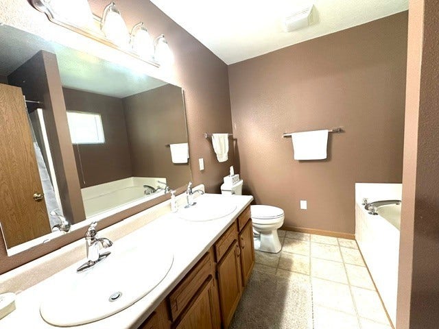 1712 Austin Drive, Lebanon, IN 46052 Dual-sink vanity with wood-finish cabinetry, a large wall-mounted mirror, and an integrated soaking tub