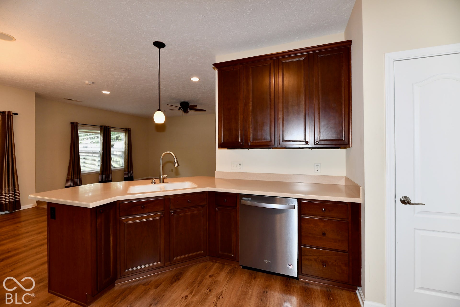 U-shaped kitchen counter with an integrated sink, dark wood-finish cabinetry, stainless steel dishwasher, and wood-finish flooring