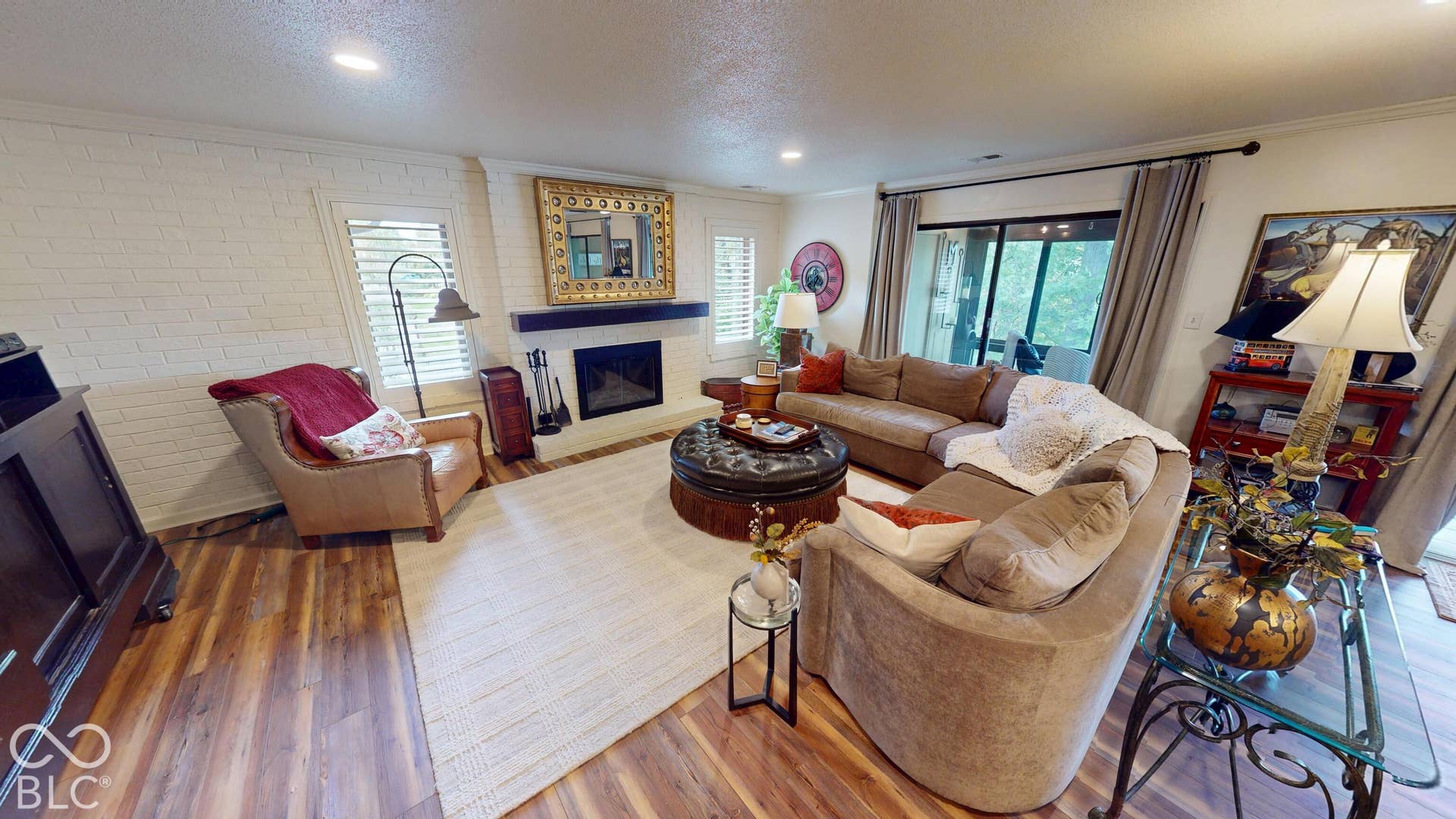 201 Bluffs Circle, Noblesville, IN 46062 Living area featuring wood-finish flooring, a white brick accent wall, and a fireplace with a dark wood mantel
