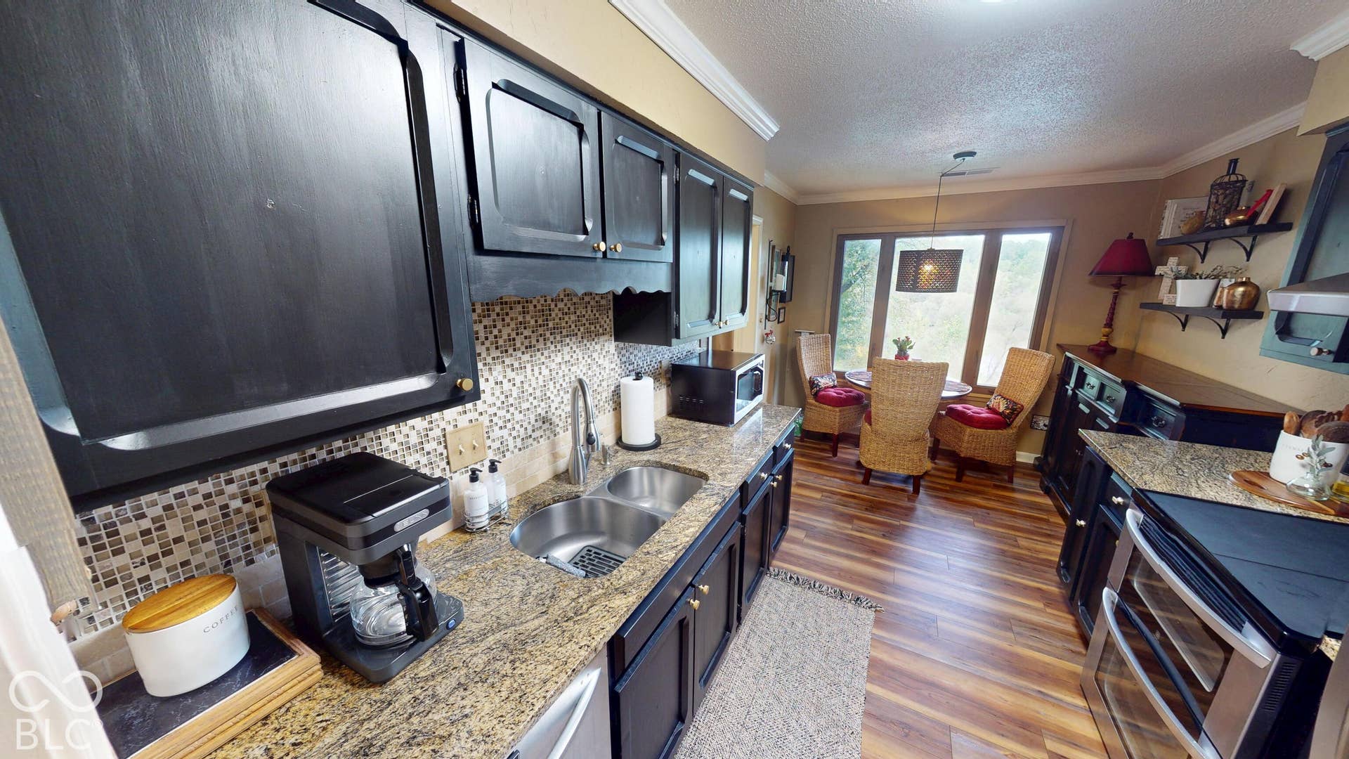 201 Bluffs Circle, Noblesville, IN 46062 Kitchen featuring wood-finish flooring, dark cabinetry with gold-tone hardware, a mosaic tile backsplash, and stone-finish countertops