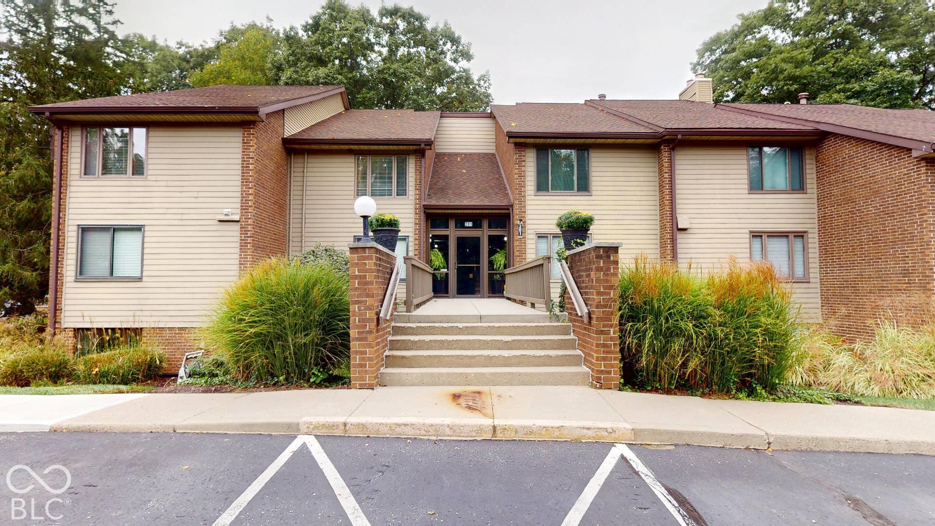 201 Bluffs Circle, Noblesville, IN 46062 Multi-level building with brick and siding exterior, featuring an entrance with concrete stairs and a wood-finish handrail, surrounded by landscaped plantings