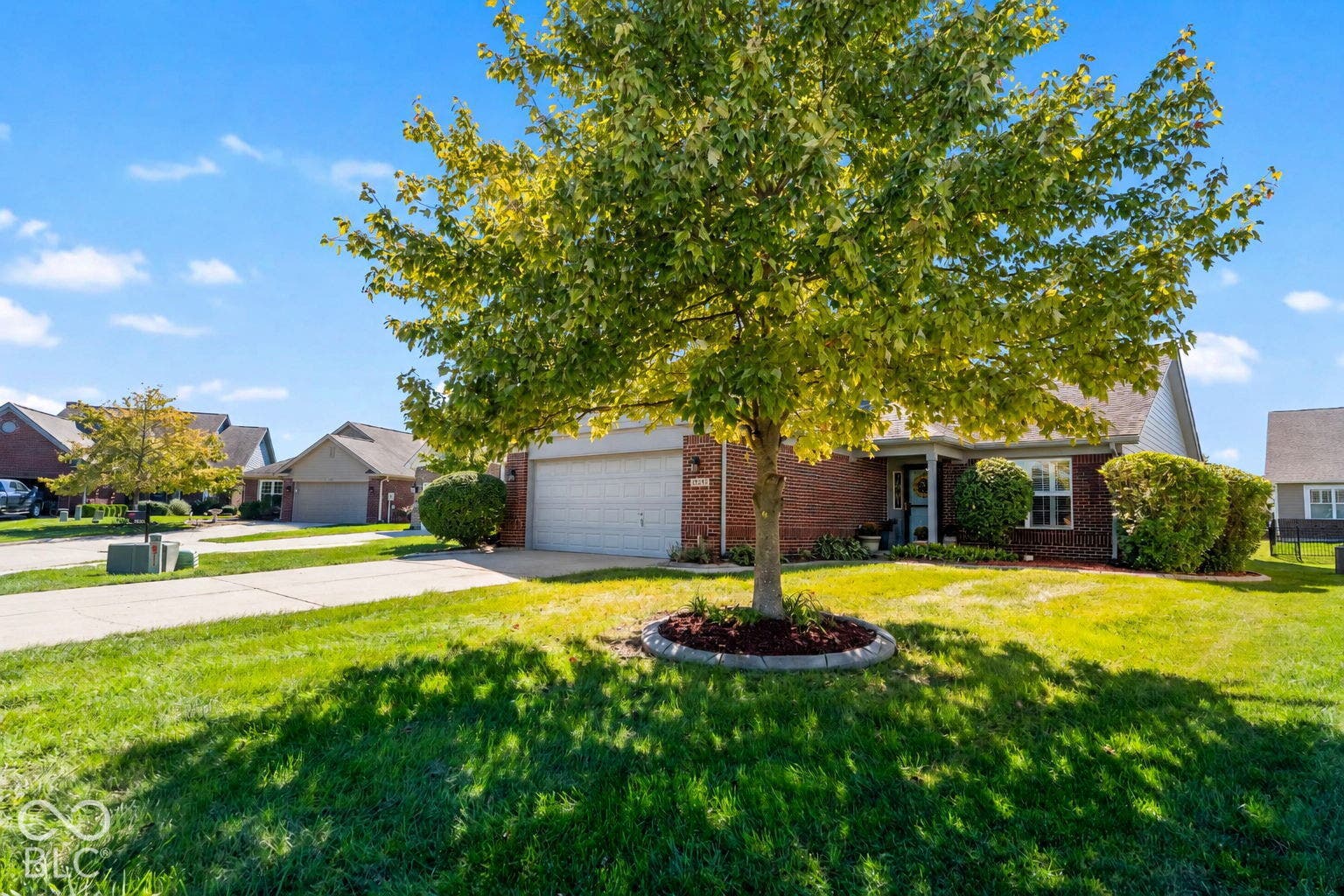 Brick exterior with white siding accents, an attached garage, a covered front entry, and mature landscaping