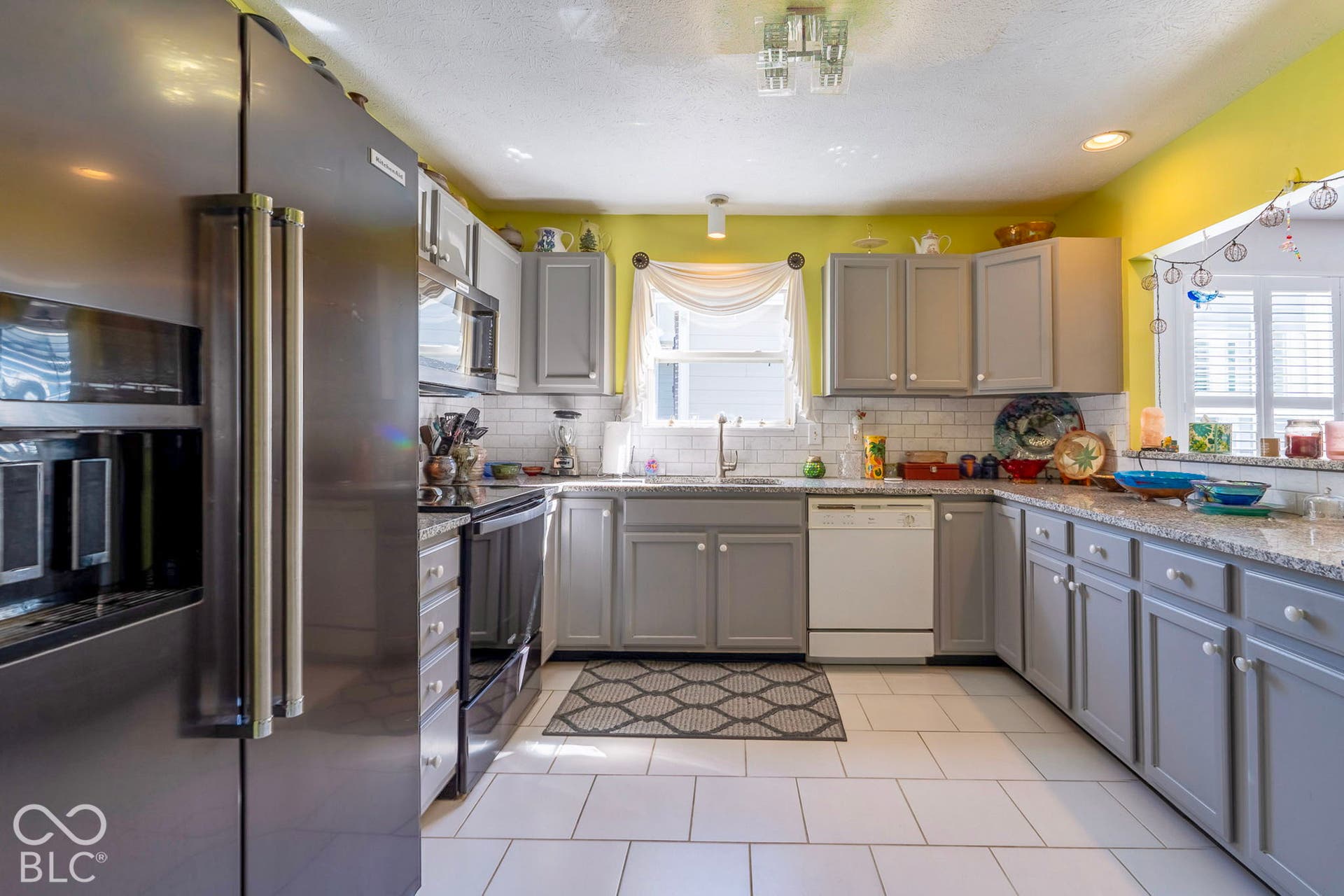 Kitchen featuring stainless steel refrigerator, white subway tile backsplash, light-colored countertops, white tile flooring, and gray cabinetry