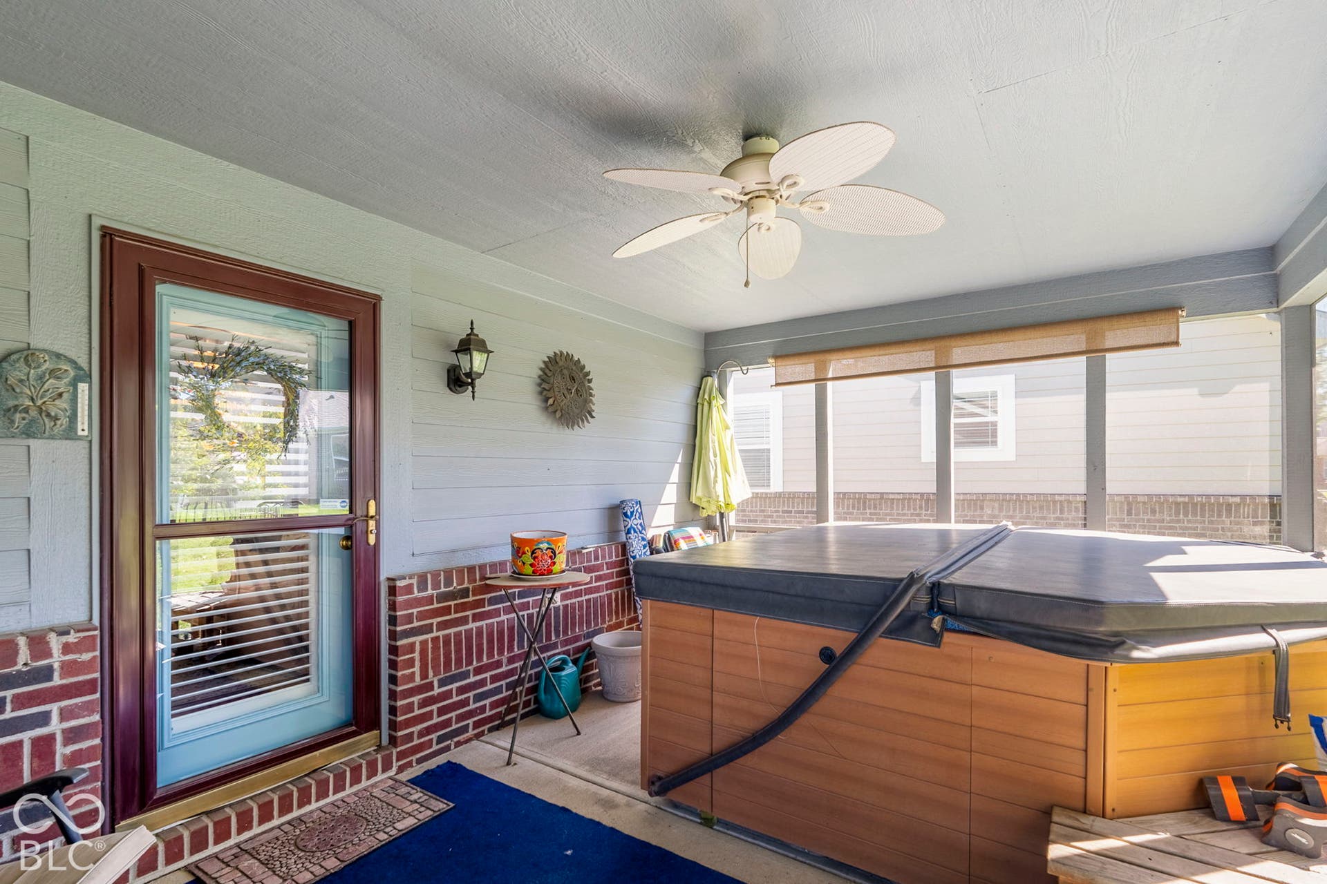 Screened porch featuring a ceiling fan, brick accent wall, and a hot tub