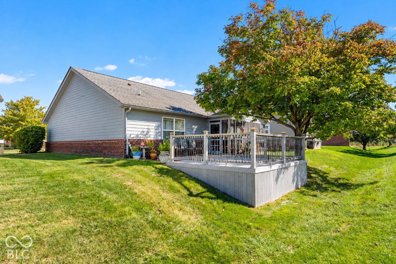 Expansive manicured lawn with mature trees, a multi-level deck, and a brick and siding exterior