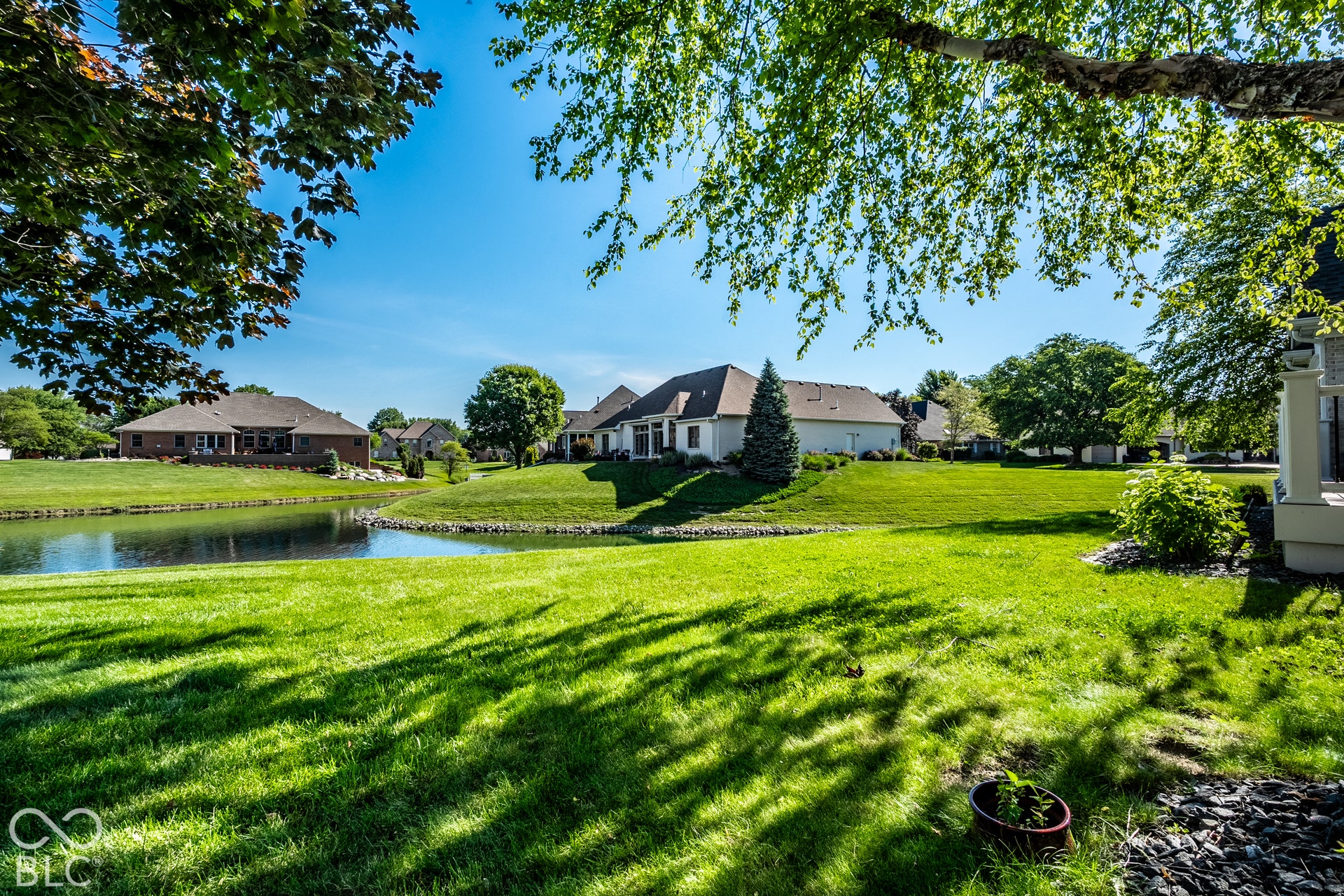 Expansive manicured lawn with mature trees, offering a private pond and a partial view of the residence with a covered patio