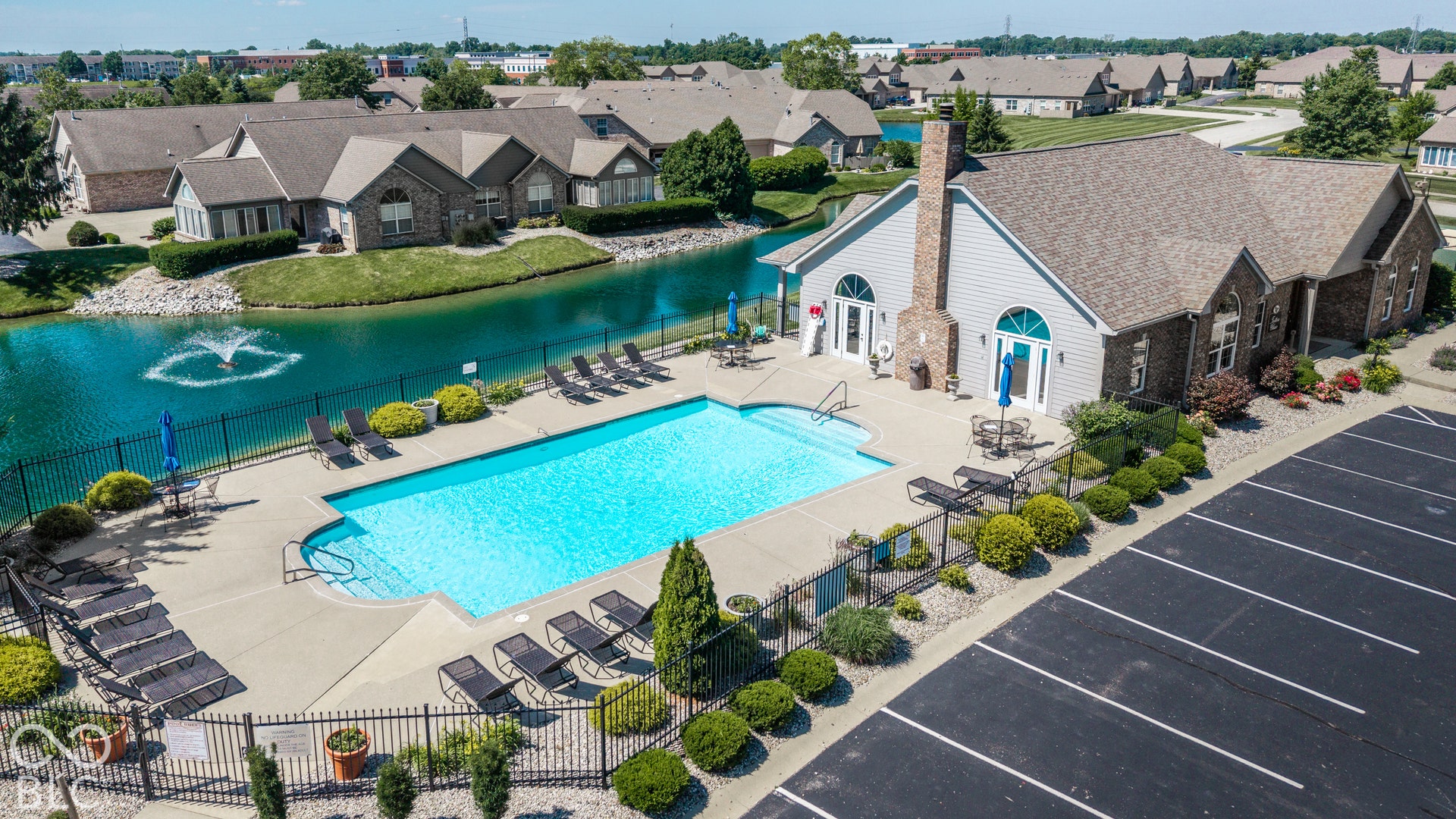 Community pool with a surrounding concrete deck, situated alongside a body of water with a fountain