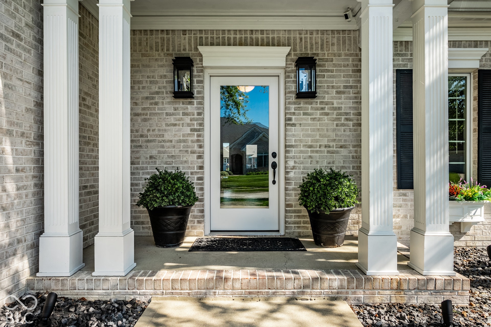 Brick exterior with a covered porch featuring fluted columns, a glass-paneled entry door, and exterior sconces