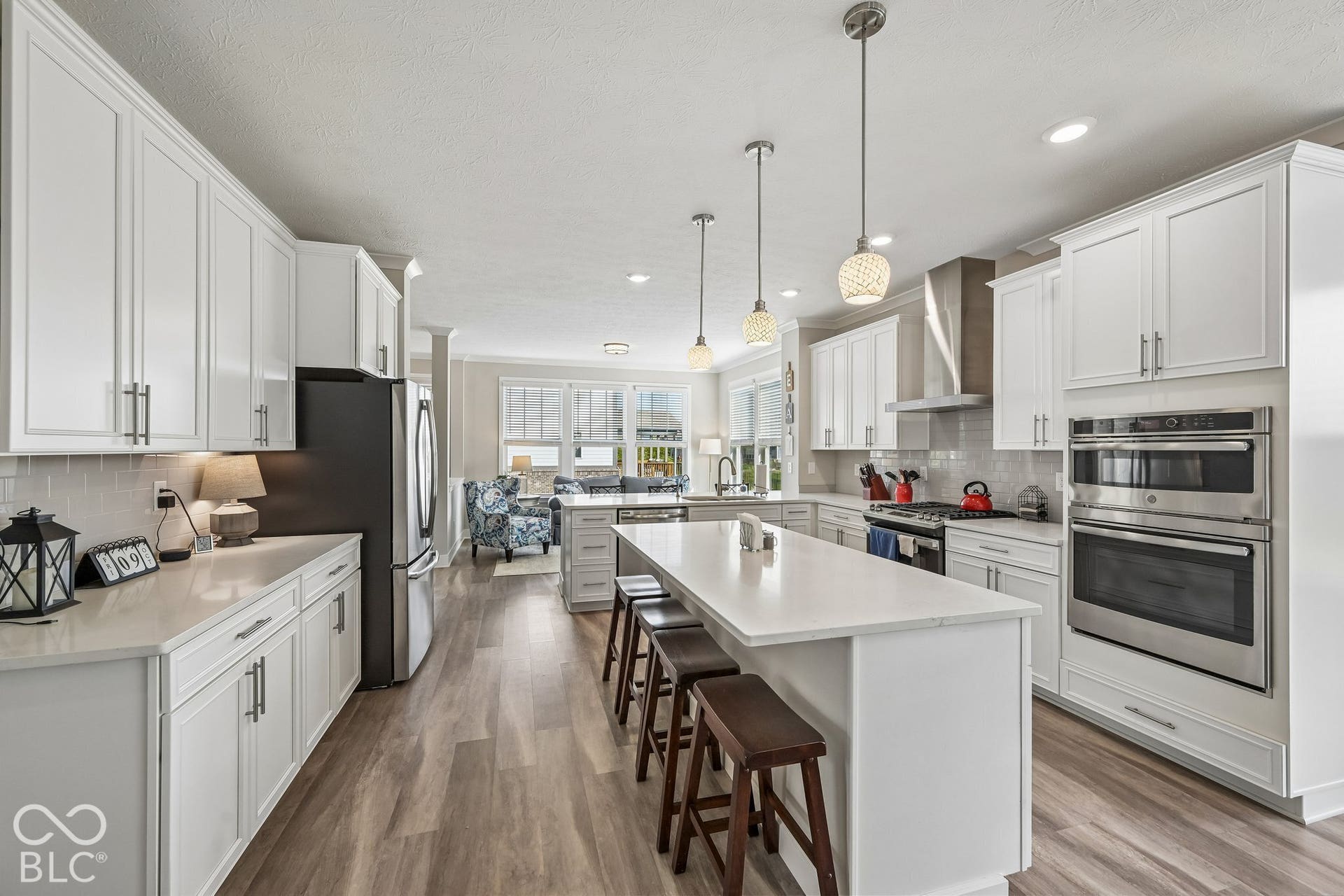 White shaker-style cabinetry, stainless steel appliances, wood-finish flooring, central kitchen island, and pendant lighting