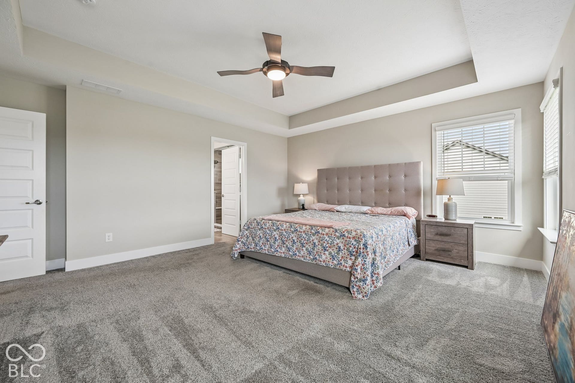 Tray ceiling, neutral wall paint, ceiling fan with integrated lighting, window with blinds, and light gray carpet