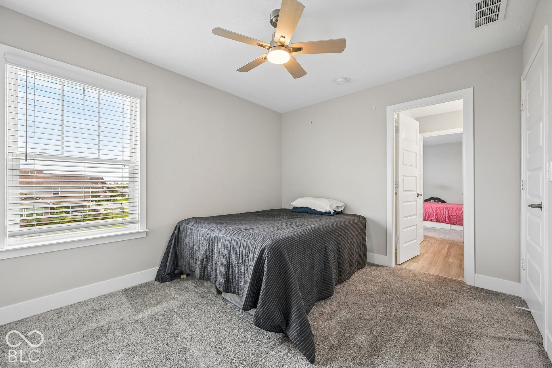 Neutral-toned walls, gray carpeting, a window with horizontal blinds, and a ceiling fan with integrated lighting