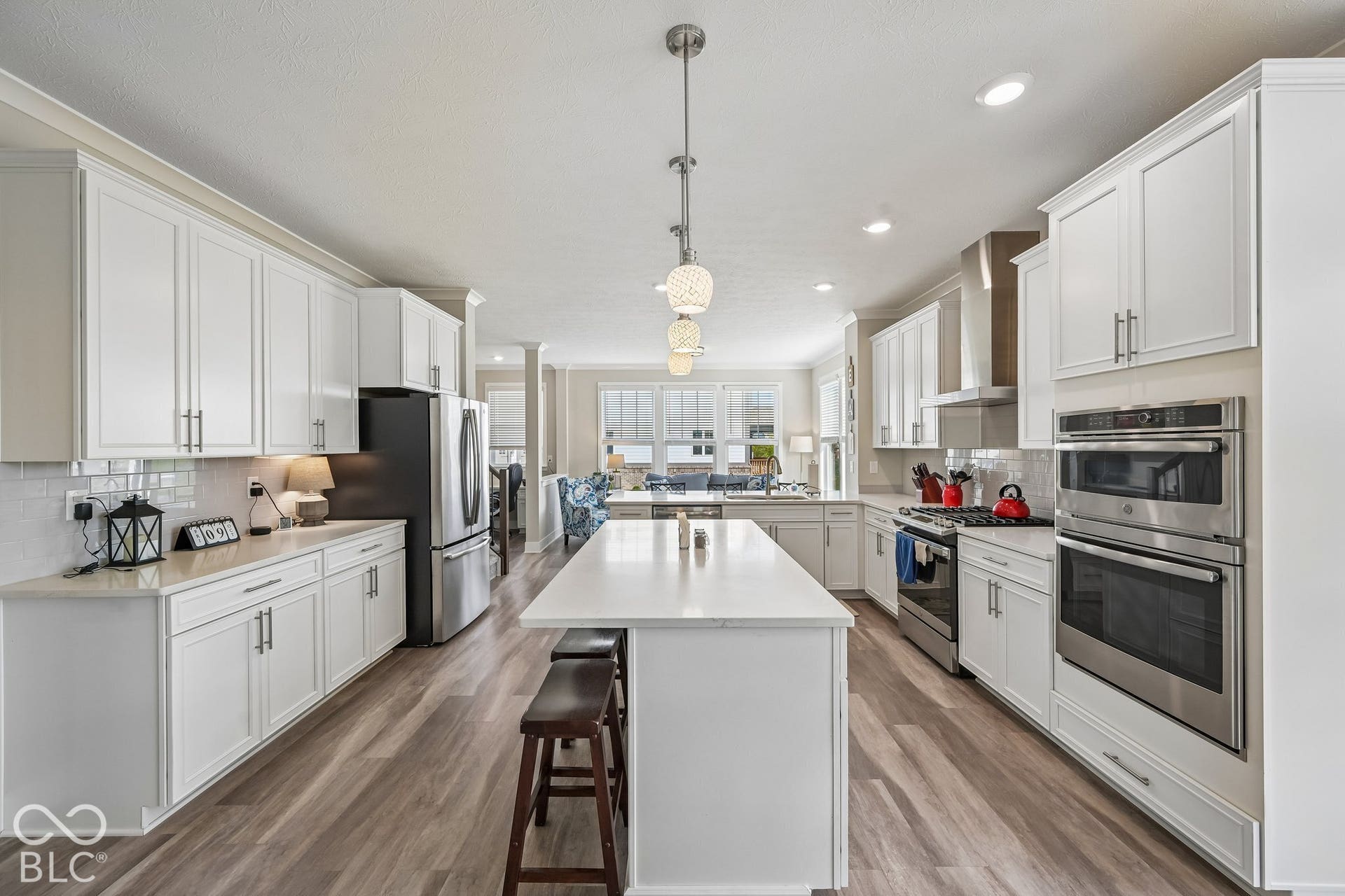 White cabinetry with brushed nickel hardware, stainless steel appliances, wood-finish flooring, central island with seating, and subway tile backsplash