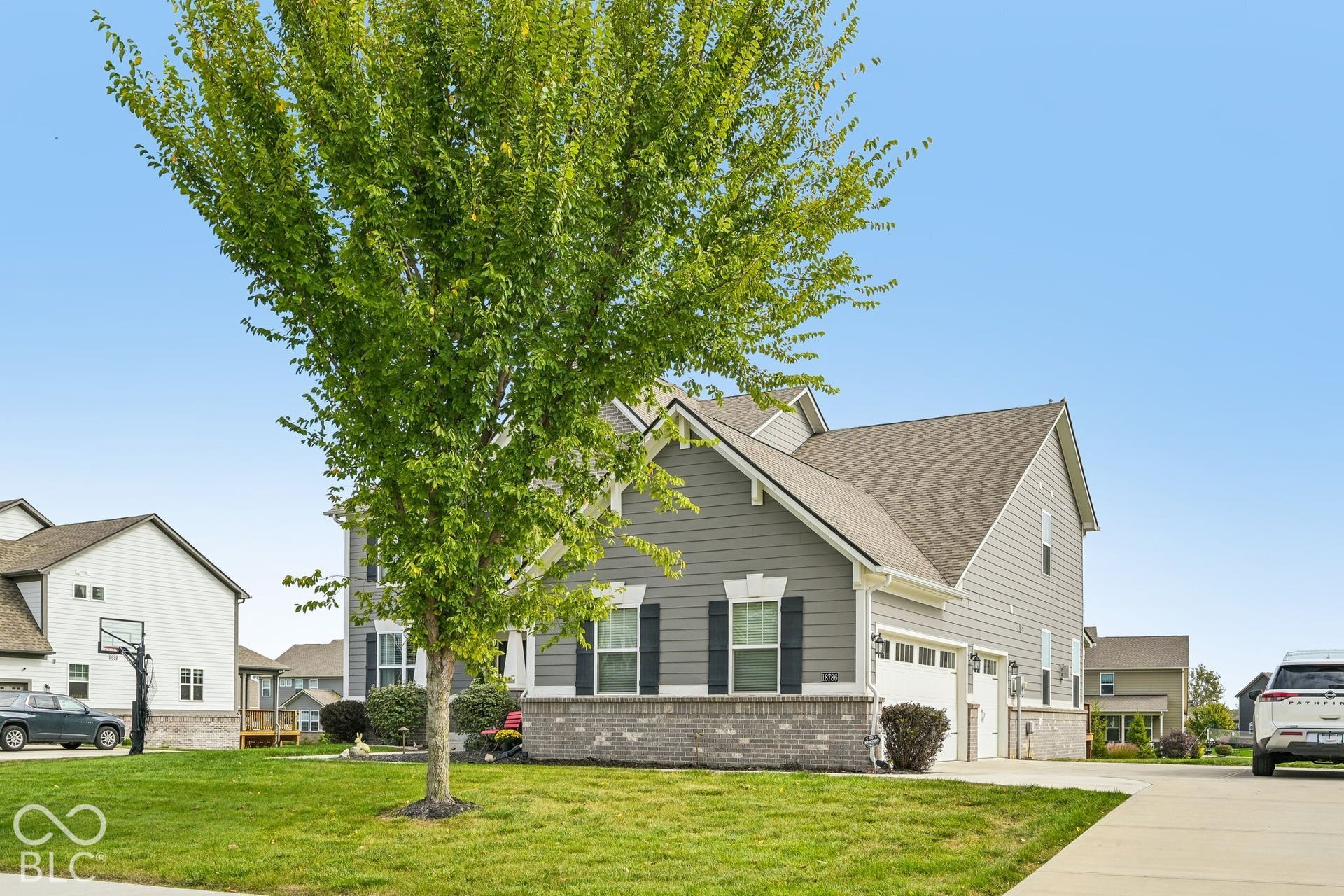 Multi-level residence featuring gray siding, a shingled roof, brick skirting, and an attached two-car garage
