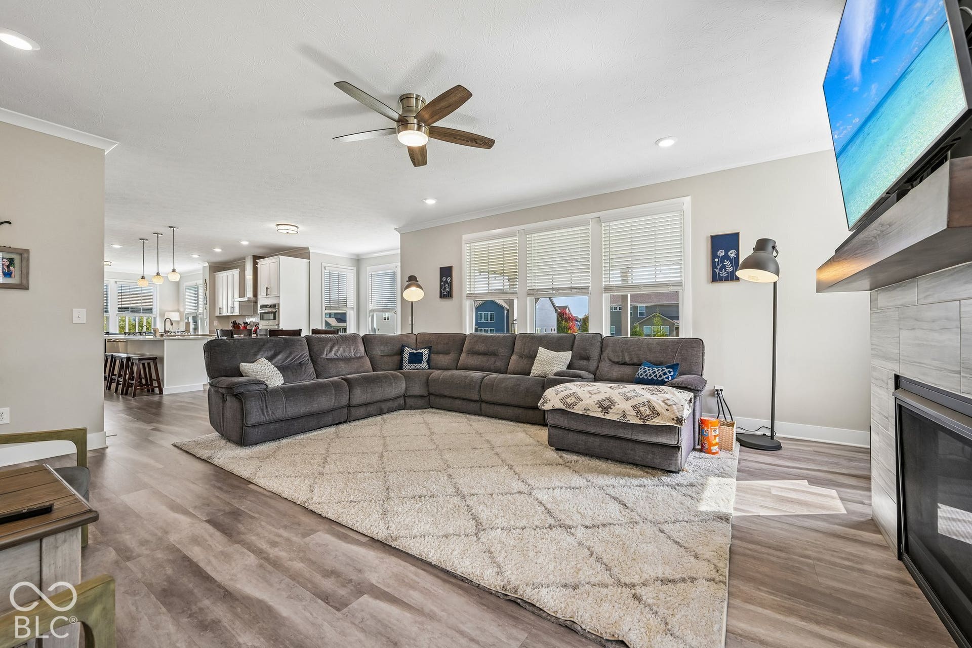 Open-concept living area featuring wood-finish flooring, a ceiling fan with integrated lighting, recessed lighting, multiple windows, and a built-in fireplace with a hearth